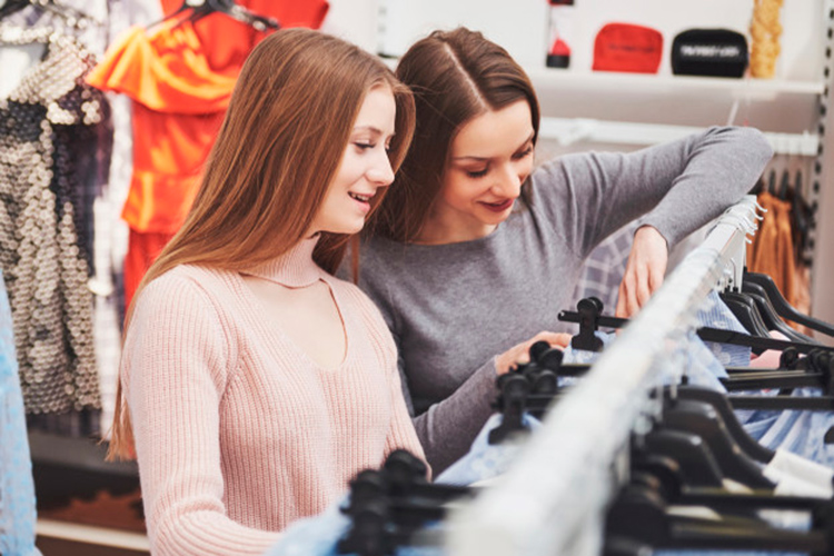 Due ragazze sorridenti che scelgono vestiti dentro ad un negozio 