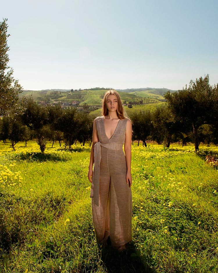 Ragazza con un vestito chiaro lungo che rispecchia la moda sostenibile ed etica in mezzo alla natura che guarda verso sinistra 