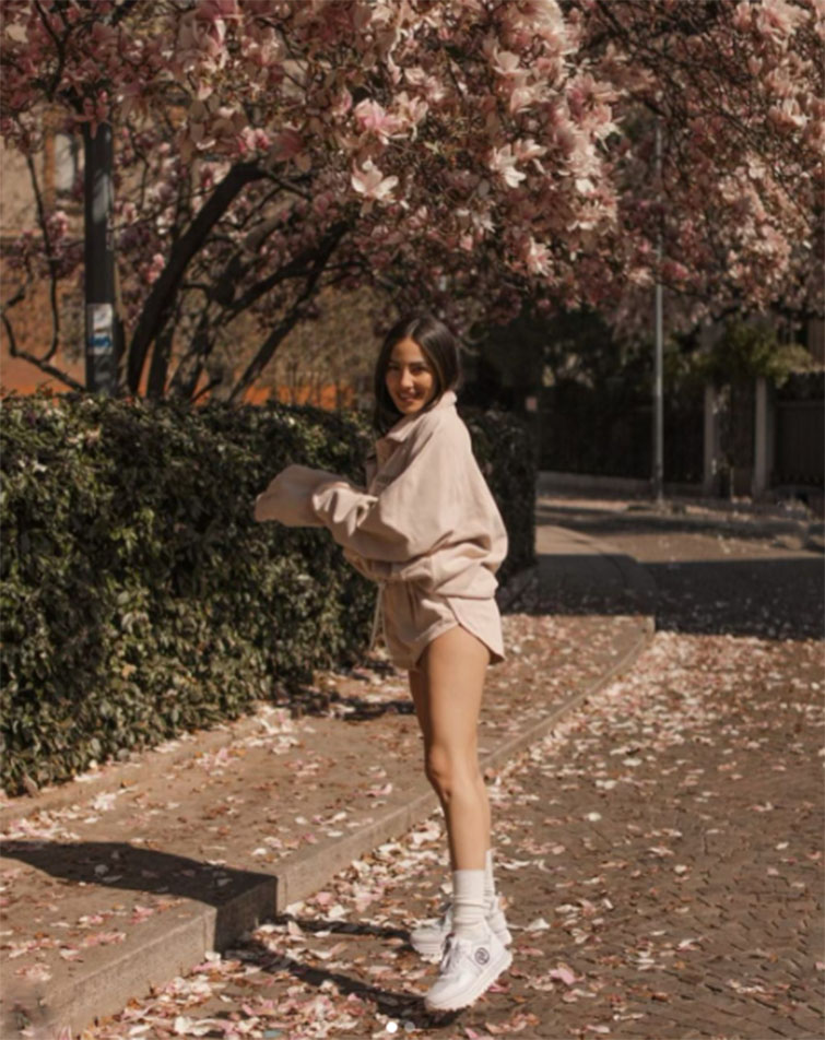 Influencer con outfit chiaro e sneakers bianca su strada alberata e con foglie