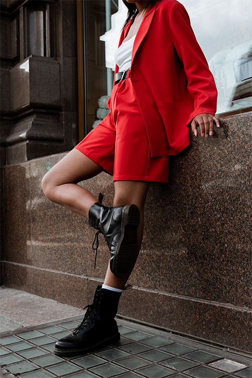 Ragazza vestita con un completo rosso e degli scarponcini neri appoggiata al muro