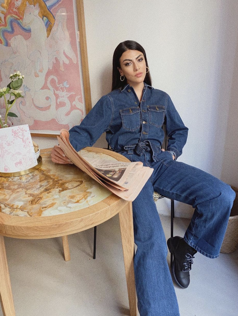 Ragazza che indossa un look total jeans che legge il giornale seduta da sola ad un tavolino rotondo
