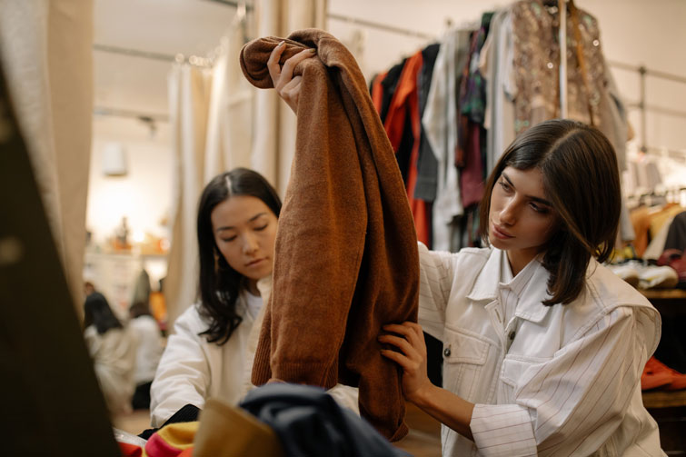 Due ragazze che stanno decidendo se comprare una giacca marrone in un mercatino di abbigliamento usato a Torino