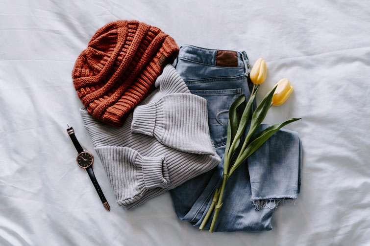 outfit di uno dei migliori marchi ecologici formato da un cappello, un maglione, jeans, orologio ed un mazzo di fiori posizionati su un lenzuolo