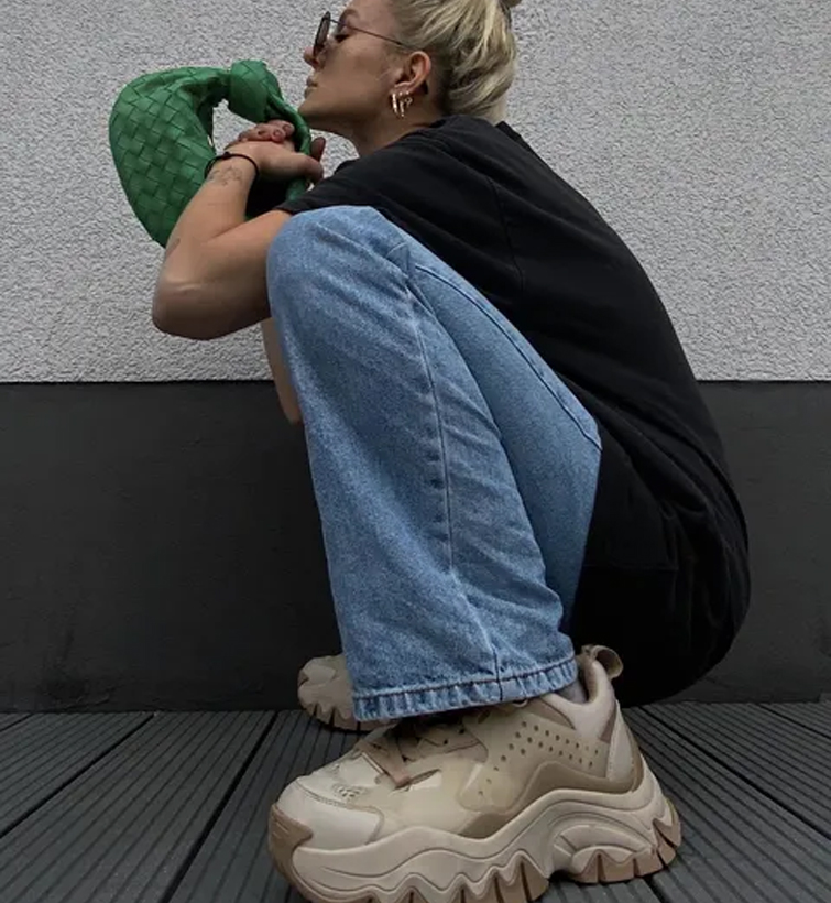 influencer Marina Themoss in posa in ginocchio mentre indossa dei jeans, una maglietta nera, una borsa verde e delle scarpe XXL, una delle sneakers da donna 2022