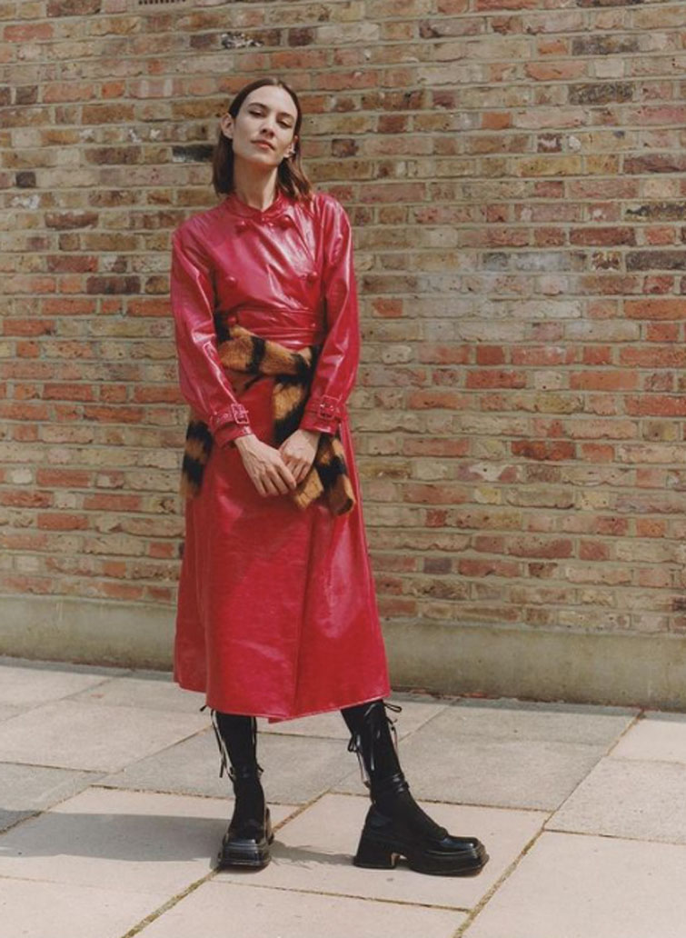 Alexa Chung, una delle influencer più seguite al mondo, in posa davanti ad un muro di mattoncini indossando un vestito rosso di pelle