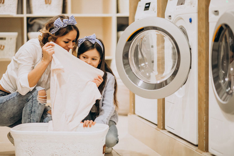 madre e figlia mentre fanno il bucato in una lavanderia a gettoni e annusano un lenzuolo bianco lavato in una delle lavatrici all’ozono